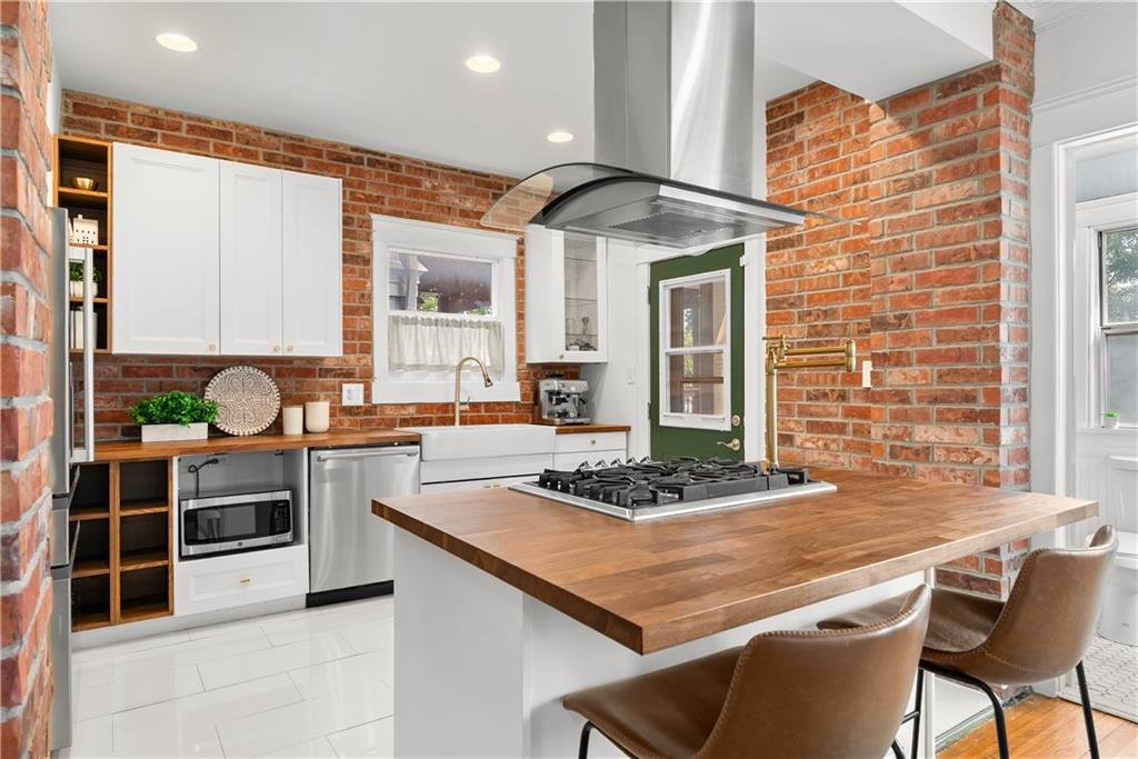 Kitchen with exposed brick walls, white cabinetry, and a butcher-block island with a gas cooktop.