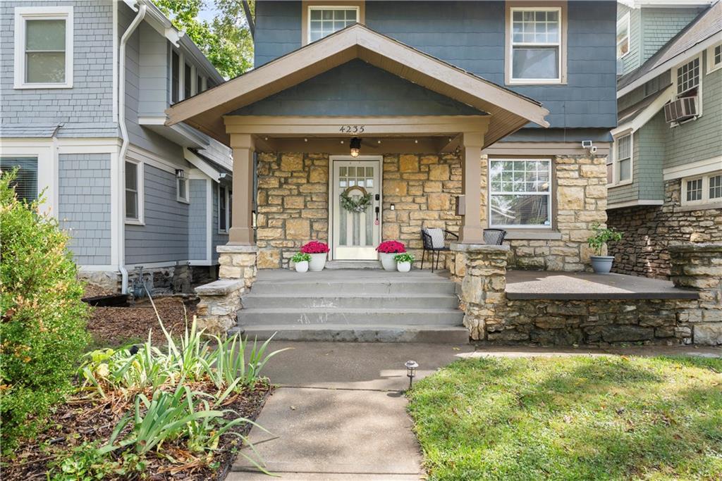 Blue two-story house with a stone façade, covered porch, and flower pots by the entrance.