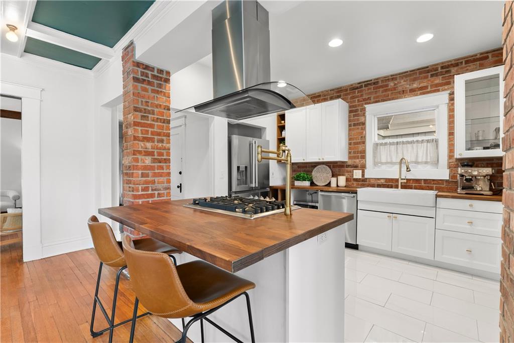 Kitchen with exposed brick, white cabinets, and a wood-topped island with a gas cooktop.