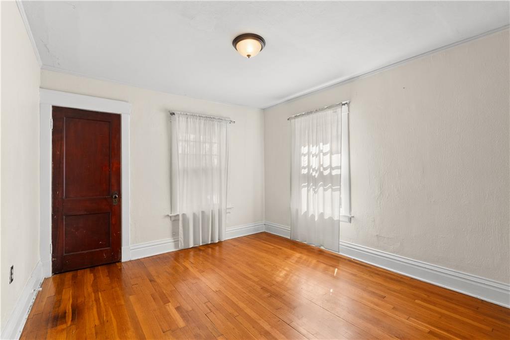 Empty room with polished hardwood floors, two curtained windows, and a dark wood door.