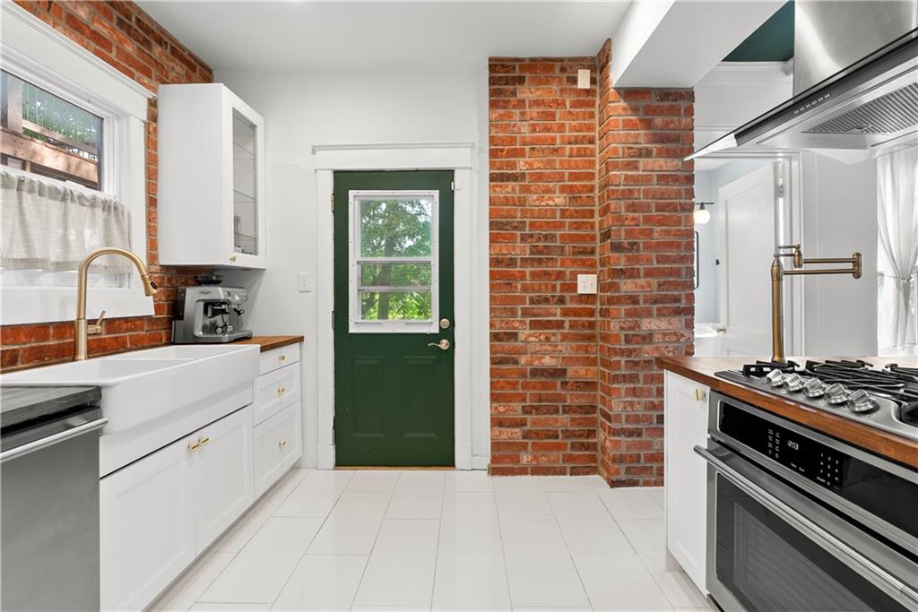 Kitchen with exposed brick walls, a farmhouse sink, stainless steel range, and dark green door.