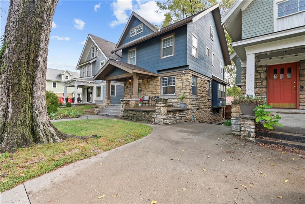 Blue two-story house with a stone facade and covered porch beside a large tree.