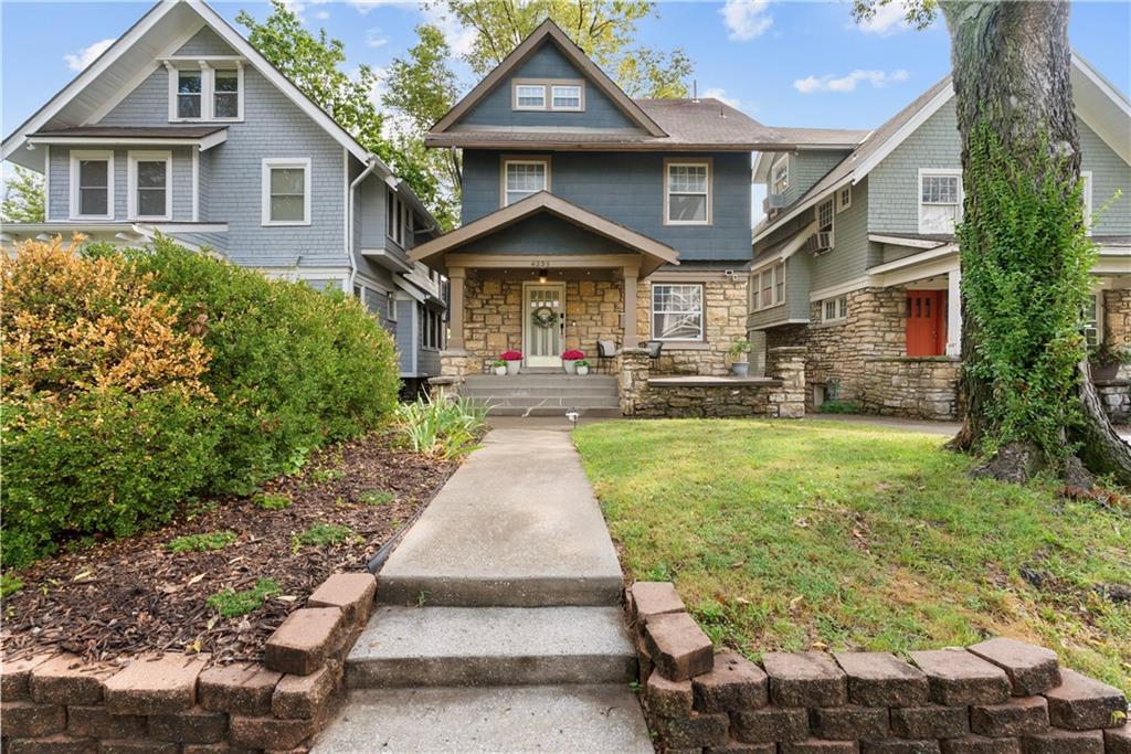 Gray-blue two-story house with a stone facade, front porch, and walkway through the yard.