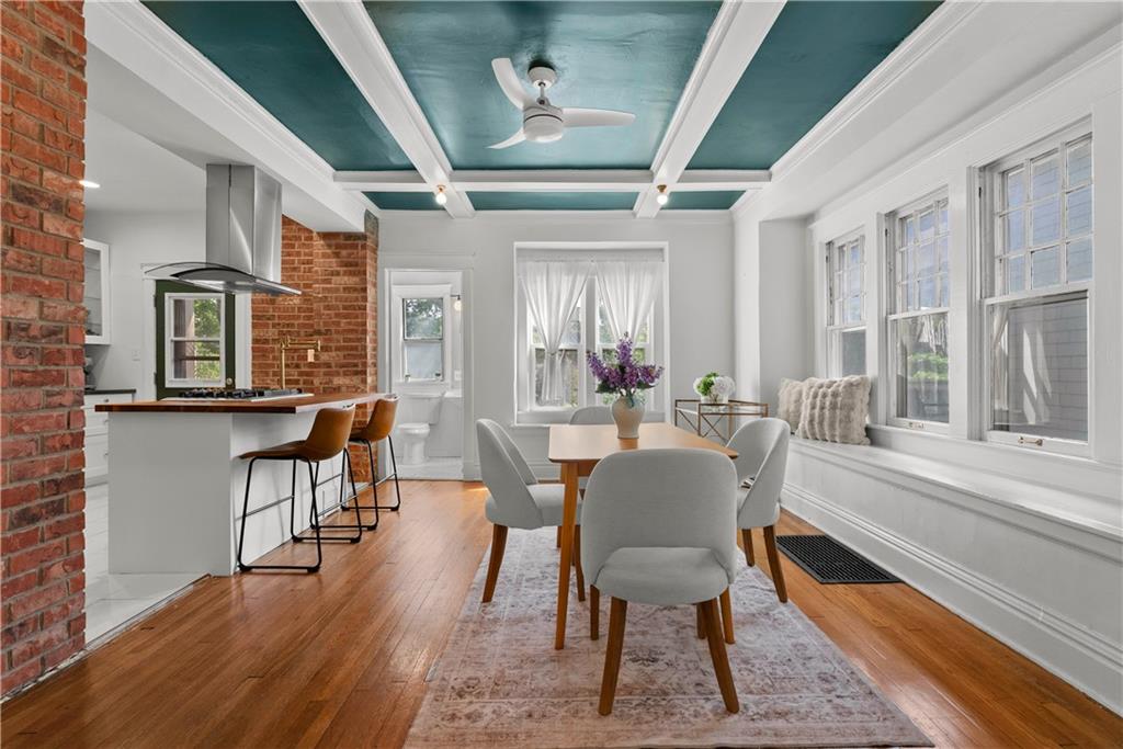 Open-plan kitchen and dining room with exposed brick, teal coffered ceiling, and hardwood floors.
