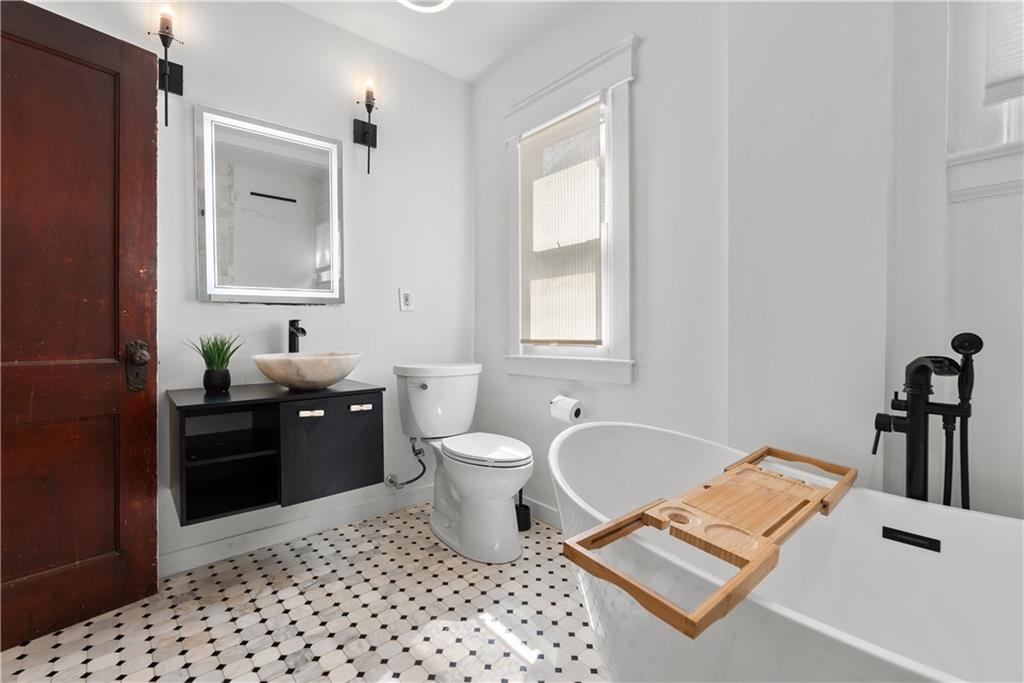 Renovated bathroom with a freestanding tub, black fixtures, floating vanity, and patterned tile floor.