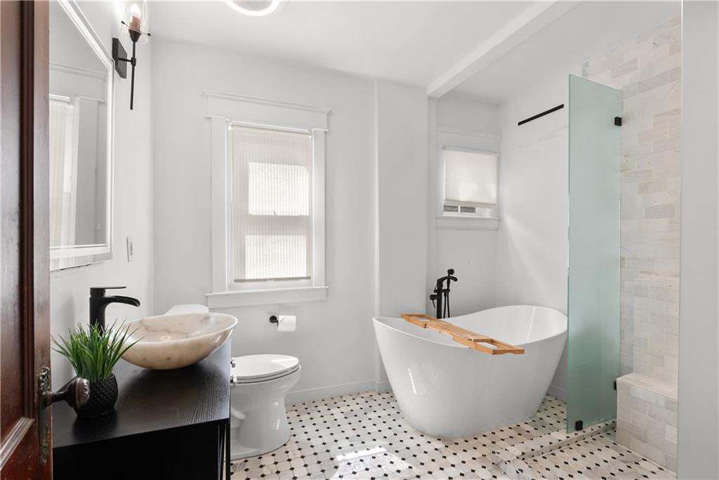Bright bathroom with a freestanding soaking tub, pale green shower glass, vessel sink, and patterned tile floor.