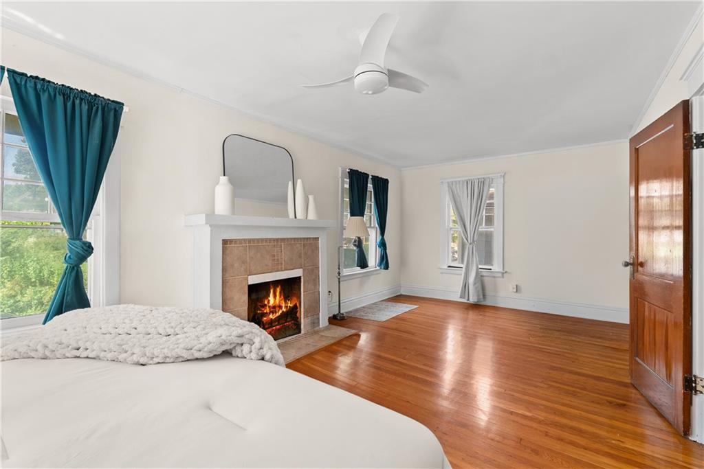 Bedroom with a tiled fireplace, polished hardwood floors, and teal curtains framing a window.