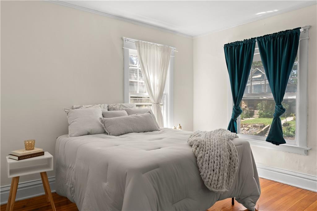 Staged bedroom with a white bed, teal curtains, and warm hardwood floors.