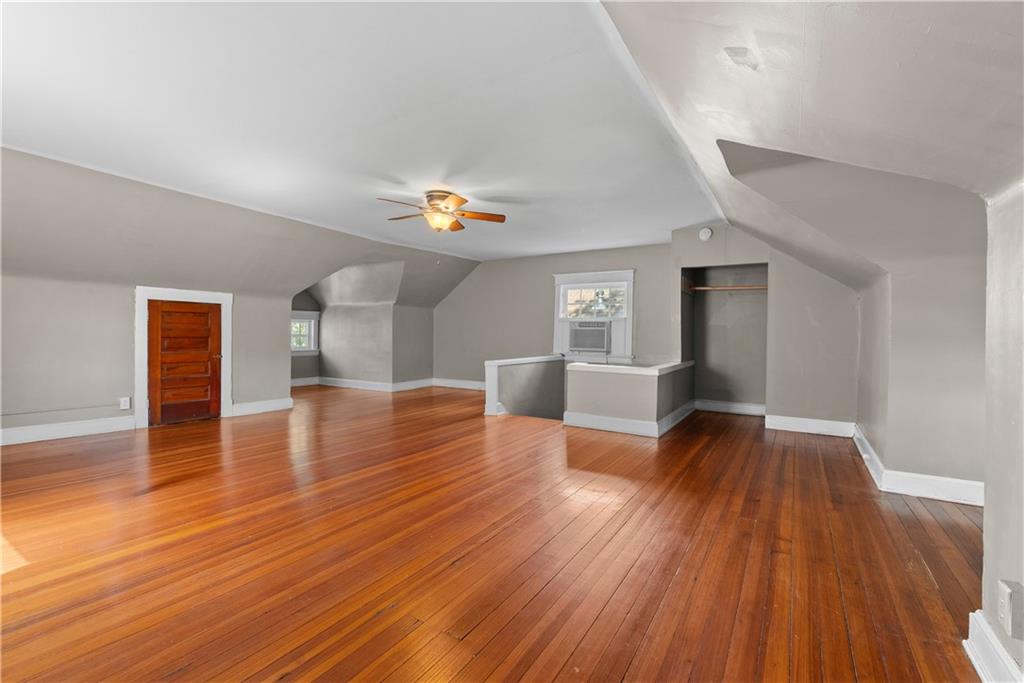 Finished attic room with polished hardwood floors, sloped ceilings, and a ceiling fan.