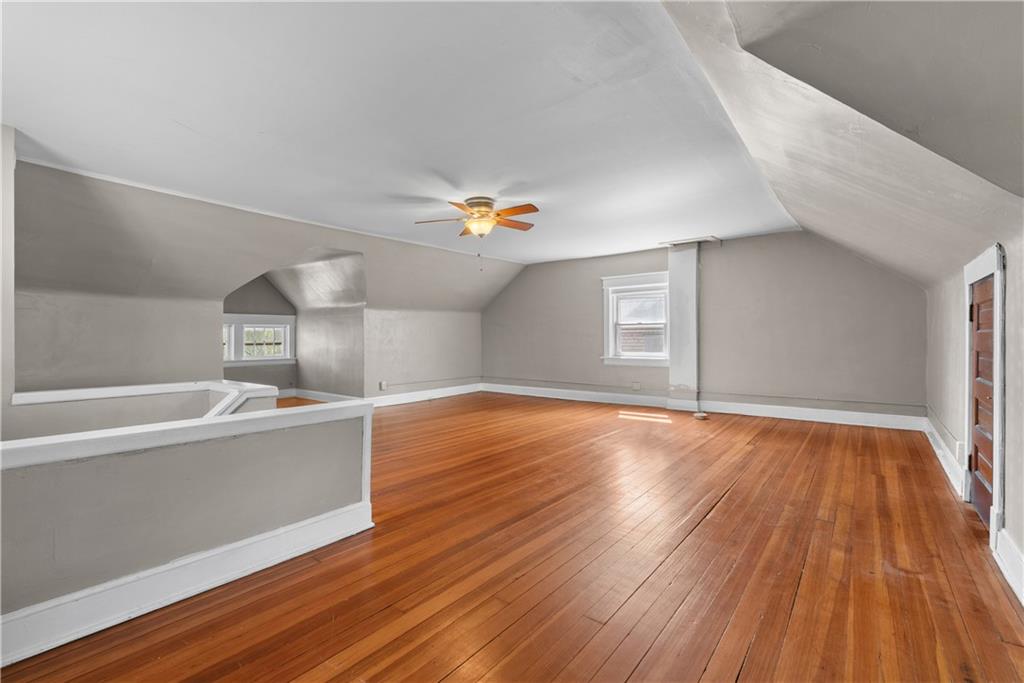 Finished attic room with sloped ceilings, hardwood floors, two windows, and a ceiling fan.