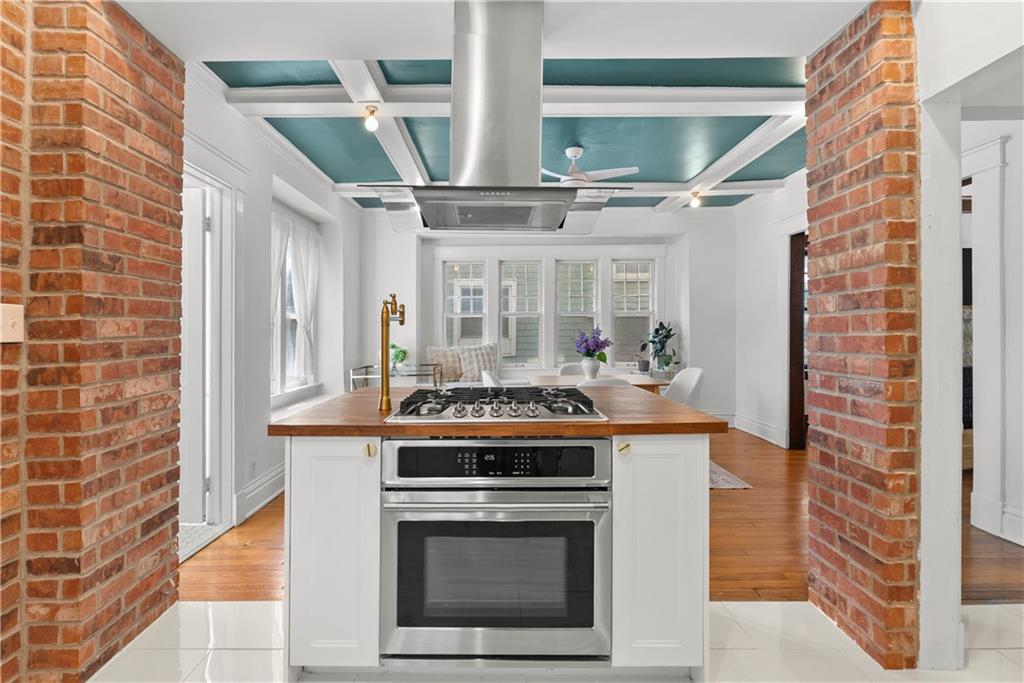 Kitchen with white island, gas cooktop, exposed brick columns, and teal coffered ceiling.