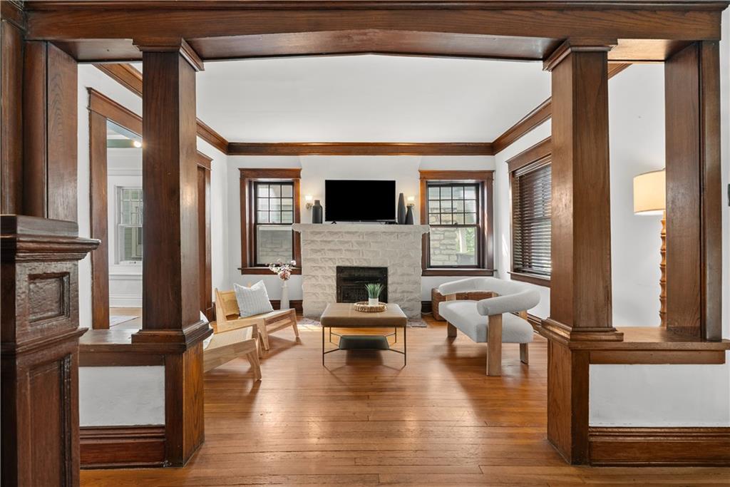 Living room with dark wood columns, hardwood floors, and a pale stone fireplace.