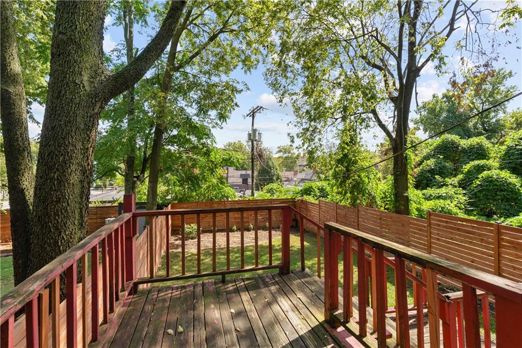 Wooden deck with red railings overlooking a fenced, tree-shaded backyard.
