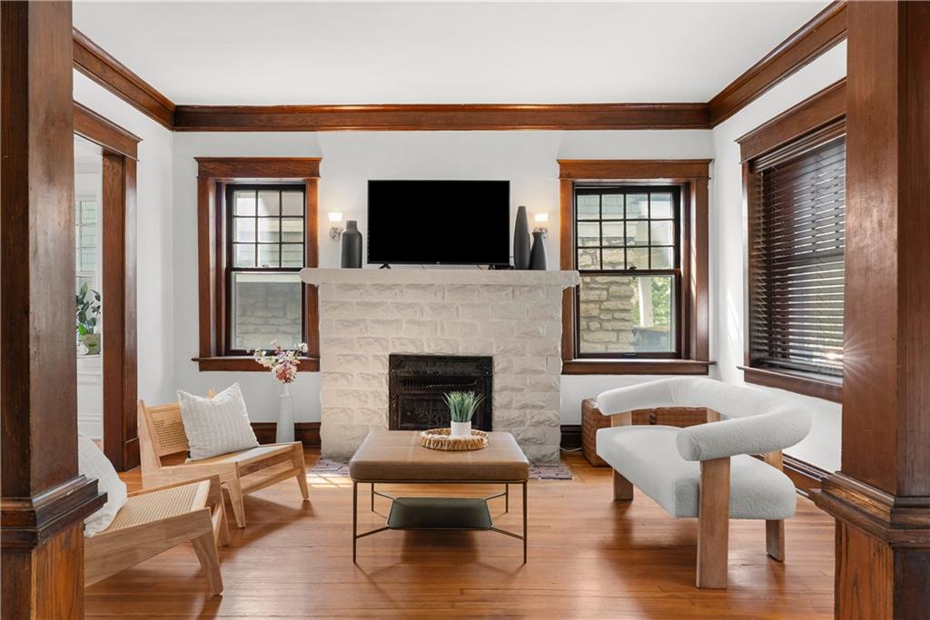 Living room with a stone fireplace, dark wood trim, tall windows, and seating.