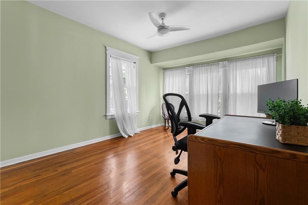 Home office with hardwood floors, a wooden desk, and large curtained windows.