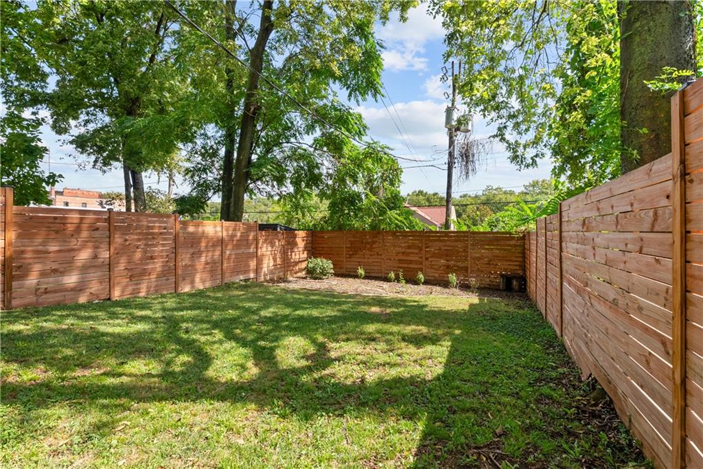 Fenced backyard with a grassy lawn and mature shade trees.