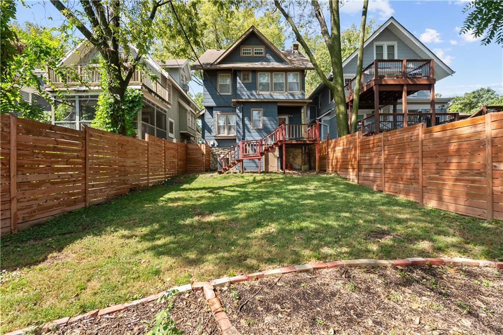 Blue two-story house with elevated wooden decks behind a grassy, fenced backyard.