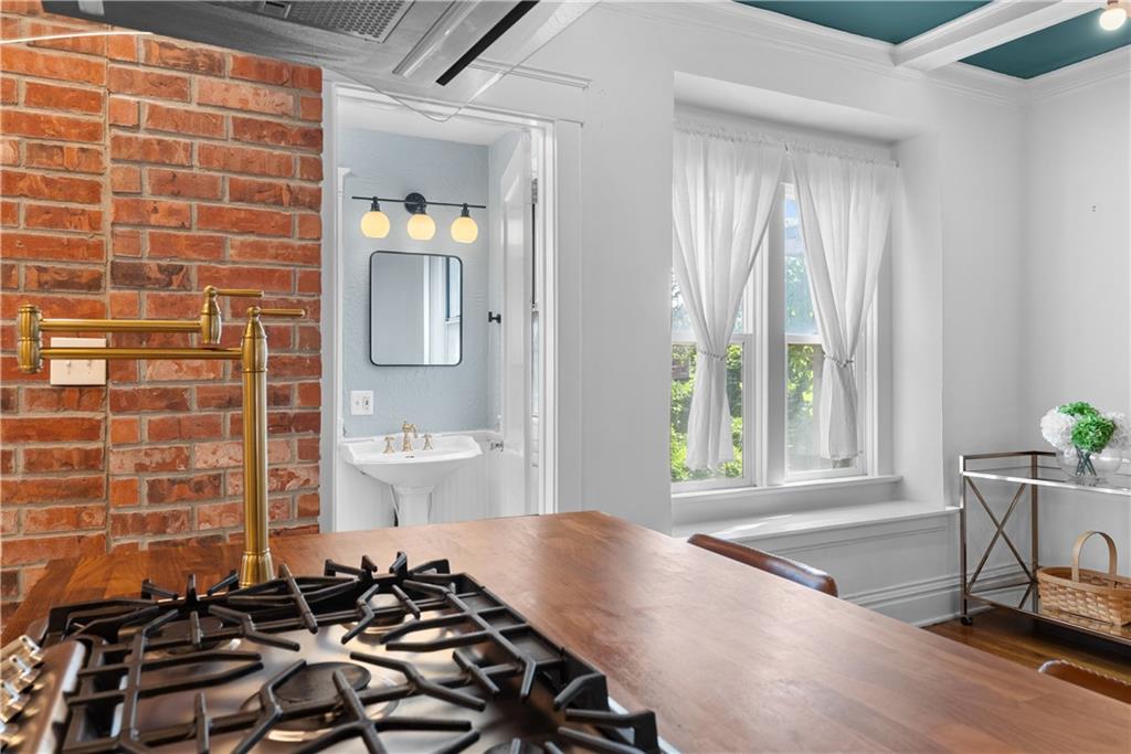 Kitchen with a wood countertop, gas cooktop, exposed brick wall, and large curtained window.
