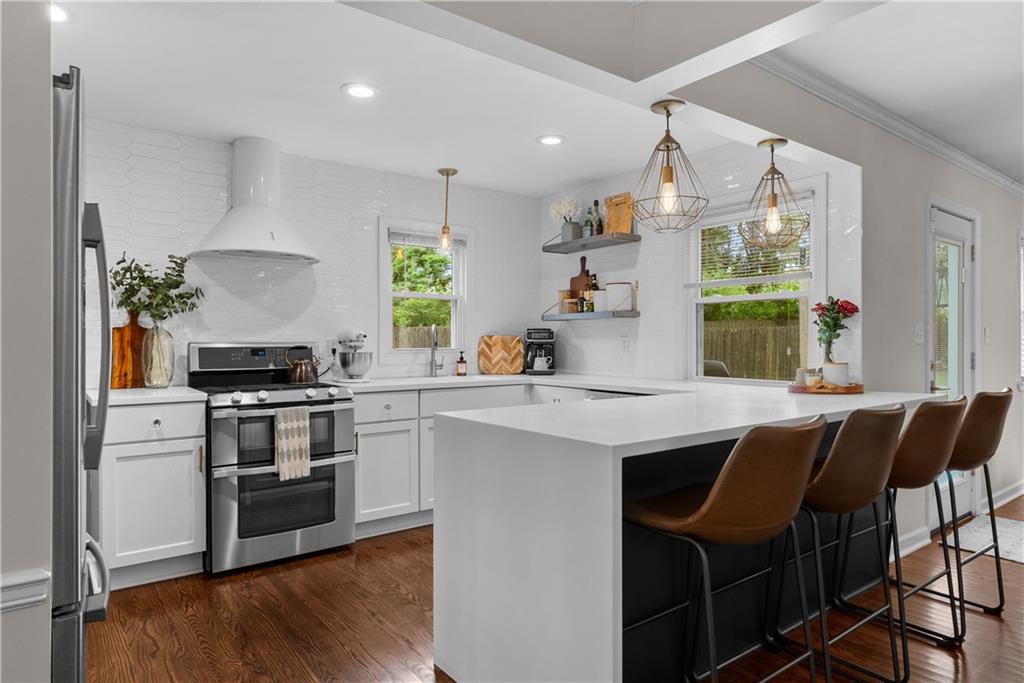 Bright white kitchen with a large island, brown bar stools, and stainless steel appliances.