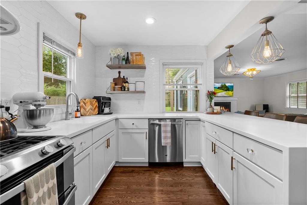 Bright white kitchen with stainless steel appliances, brass fixtures, and hardwood floors, opening to a living room.