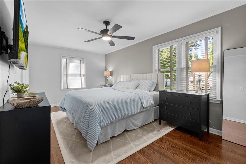 Bedroom with a king bed, gray bedding, dark dressers, and large windows with white blinds.