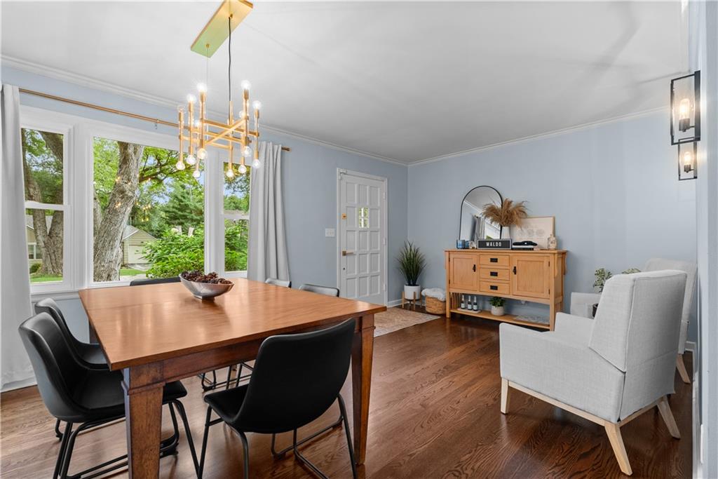 Dining room with a wooden table, black chairs, gold chandelier, and large windows overlooking leafy trees.