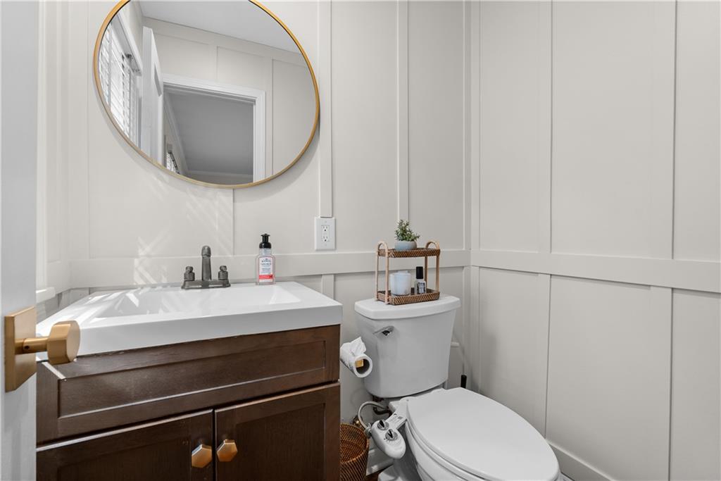 Bathroom with a dark wood vanity, round gold-rimmed mirror, and white paneled walls.