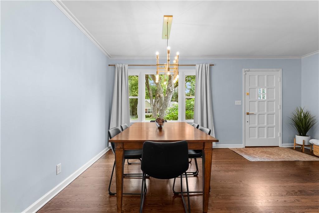 Dining room with a wooden table, pale blue walls, and large windows overlooking trees.