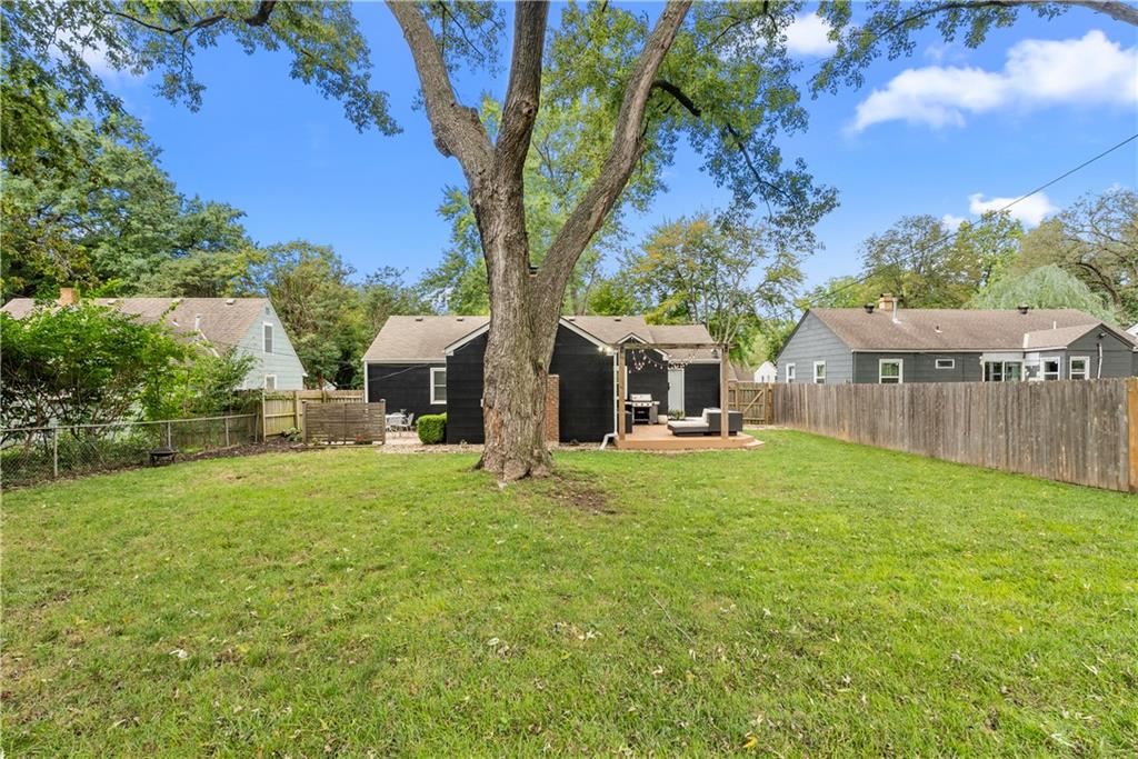 Backyard with a broad lawn, large shade tree, and covered patio with outdoor seating.