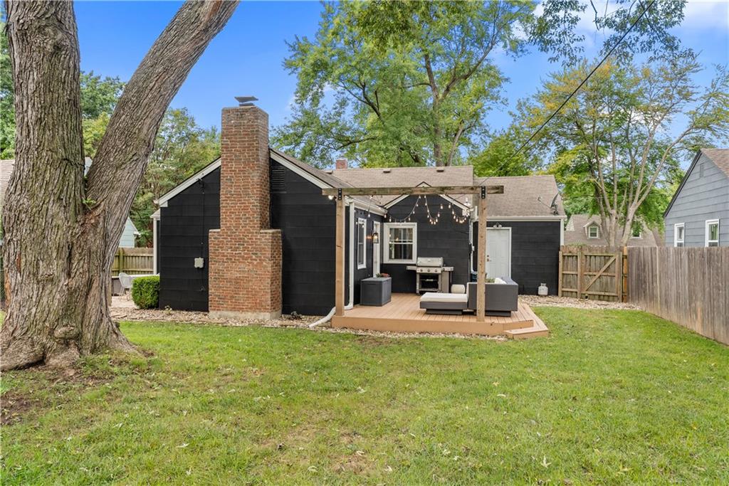 Black-sided house with a brick chimney and furnished pergola patio in a fenced backyard.