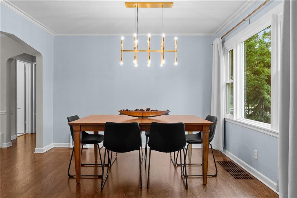 Dining room with a wooden table, black chairs, gold chandelier, and large windows overlooking trees.