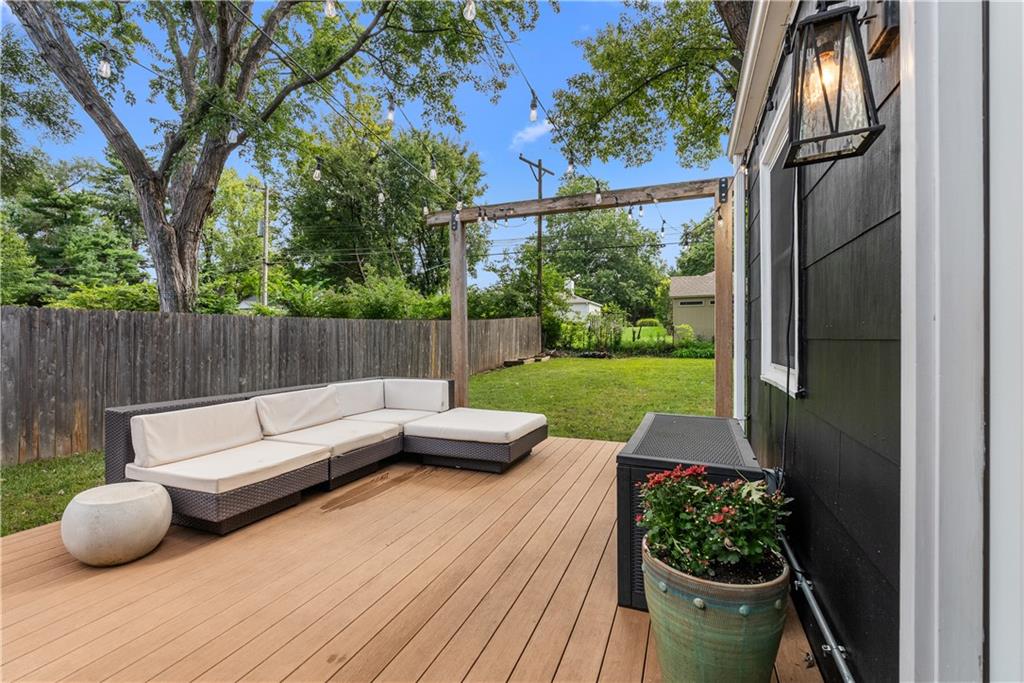 Backyard deck with sectional seating, string lights, and fenced lawn.
