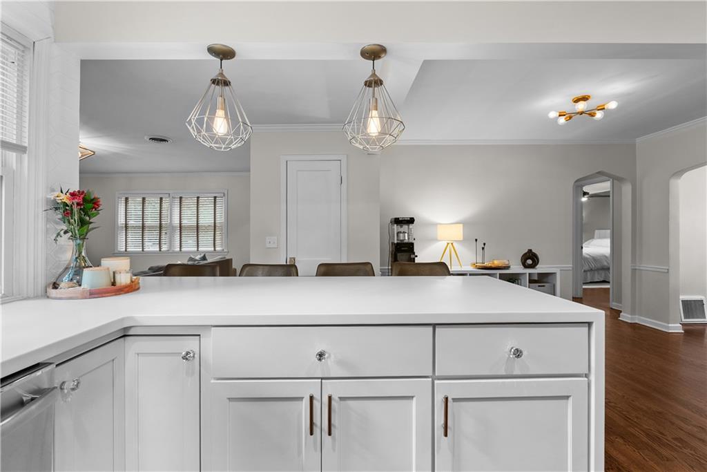 Kitchen with a large white island and geometric pendant lights, opening to a living area.
