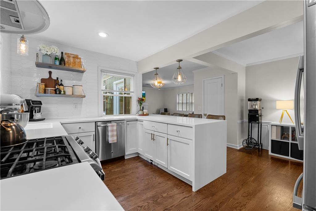White kitchen with stainless steel appliances, gas range, and dark hardwood floors opening to living area.