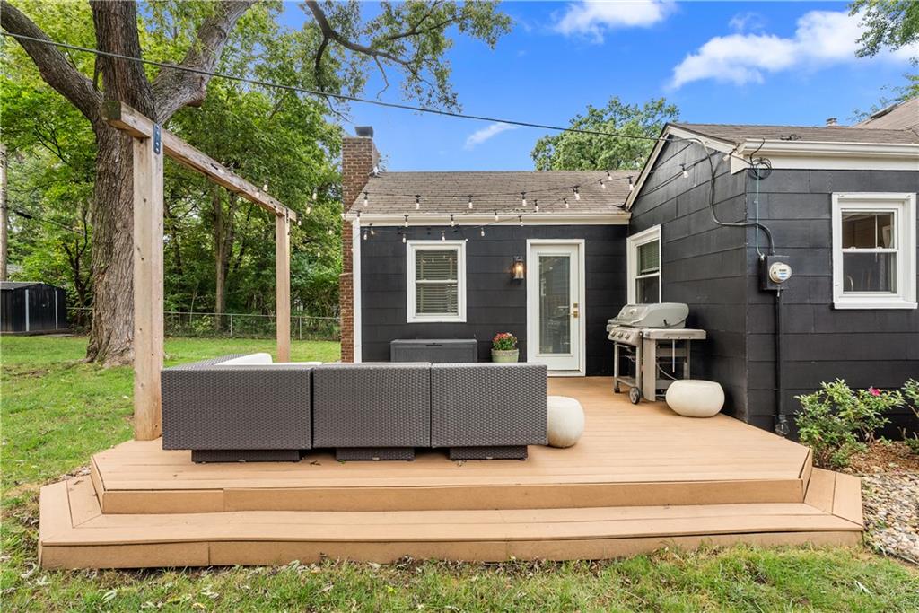 Raised wooden deck with outdoor seating and a grill beside a dark-sided home.