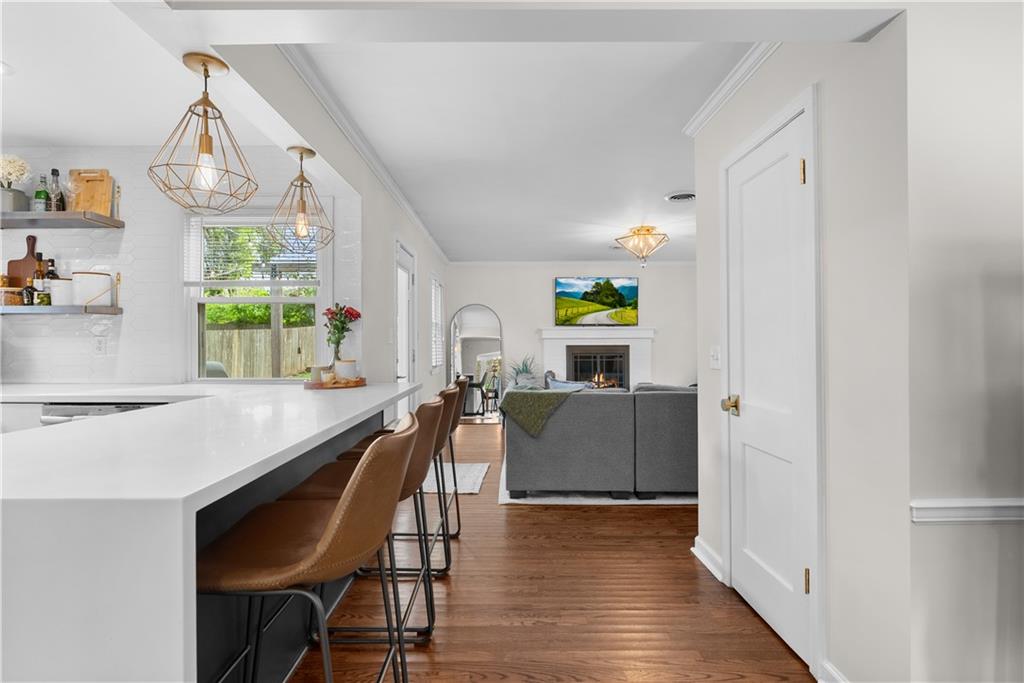 Open kitchen and living room with a white island, brown stools, and a fireplace beyond the sofa.