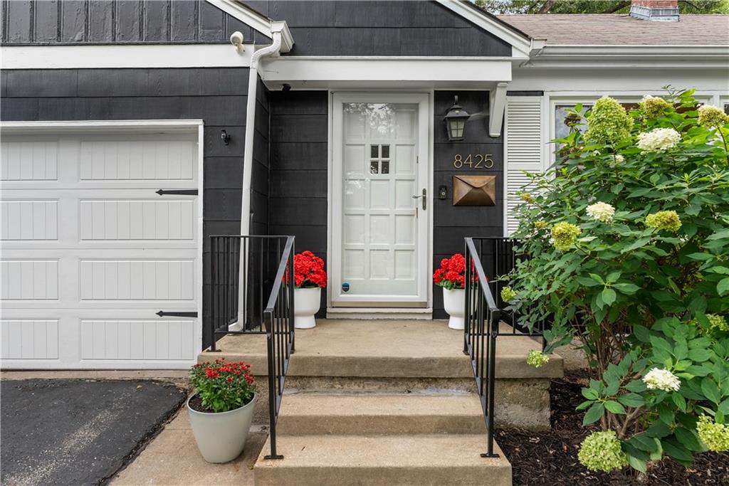House entrance with dark siding, white garage door, and flower planters beside the steps.