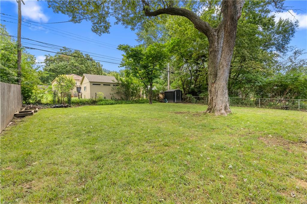 Grassy backyard with a large shade tree, fenced boundaries, and a detached garage.