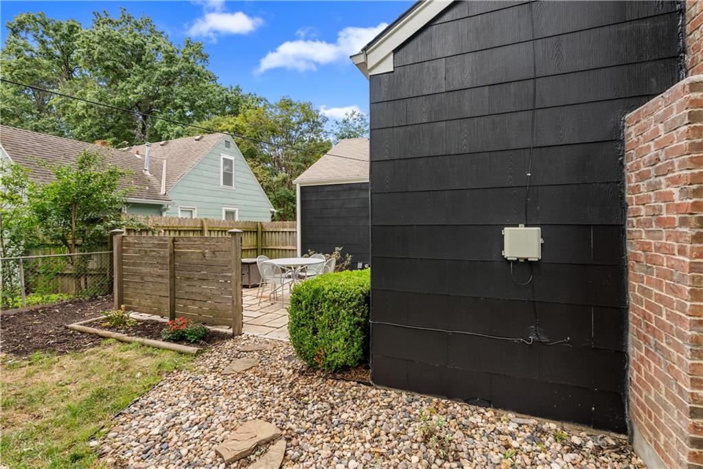 Backyard patio beside a dark-sided house, with outdoor dining furniture and a fenced garden.