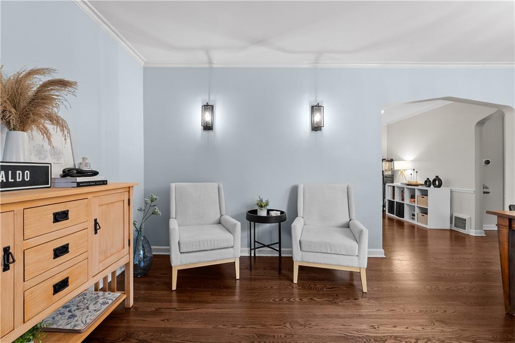 Sitting area with two light gray chairs, a round table, pale blue walls, and dark hardwood floors.