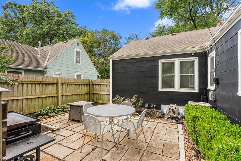 Backyard patio with a round dining set, grill, and wooden privacy fence beside a dark-sided house.