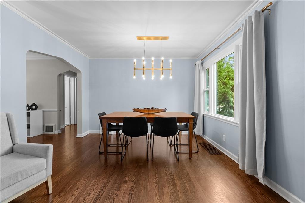 Dining room with a wooden table, black chairs, pale blue walls, and a large curtained window.