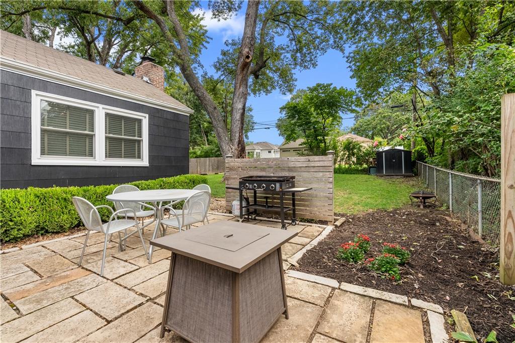 Backyard patio with outdoor dining set, fire table, and grill beside a dark-sided house.