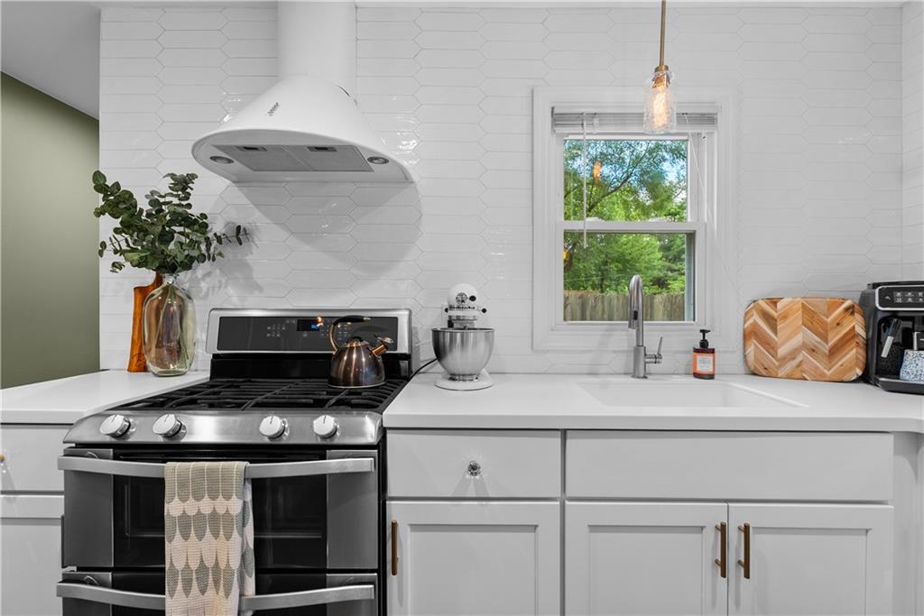Bright white kitchen with a stainless-steel gas range, hexagonal tile backsplash, and window above the sink.