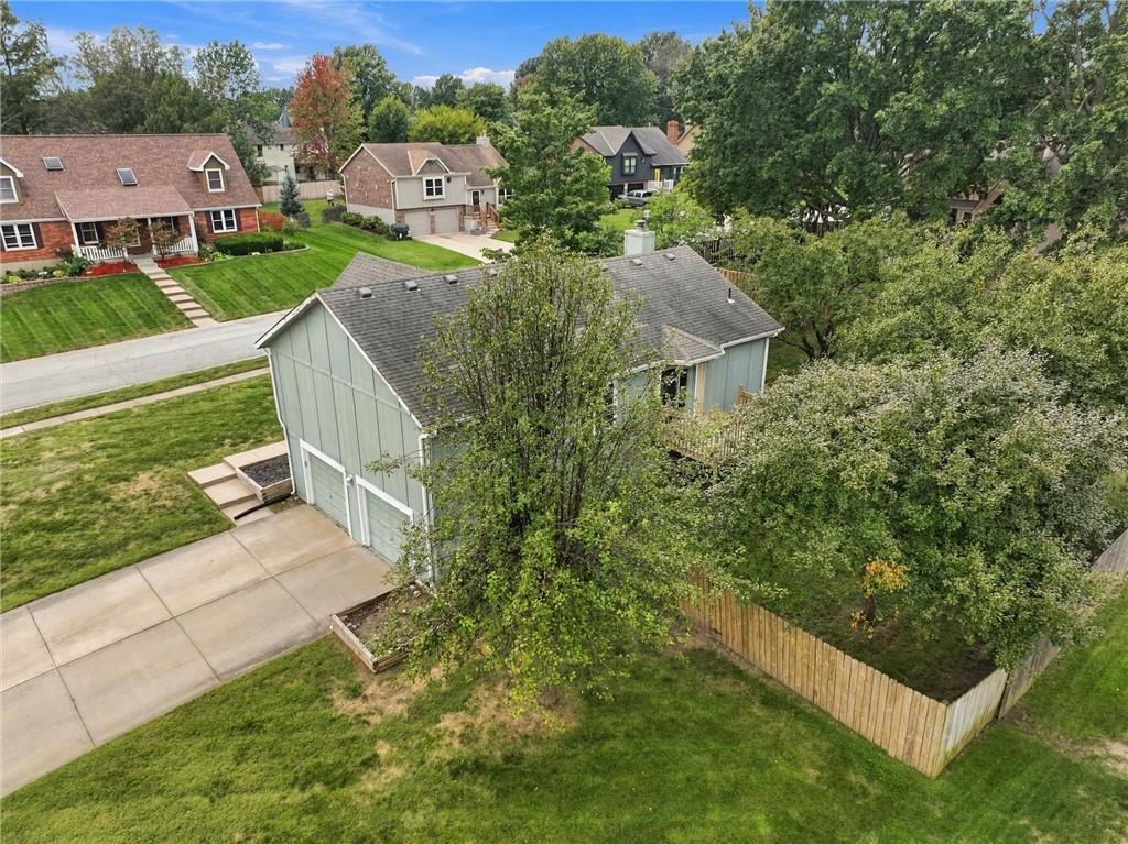 Aerial view of a gray building with two garage doors, a driveway, and a fenced grassy yard.