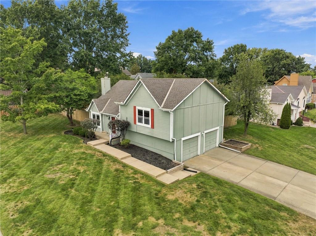 Sage-green two-story house with red shutters, multiple gables, and a wide driveway, viewed from above.