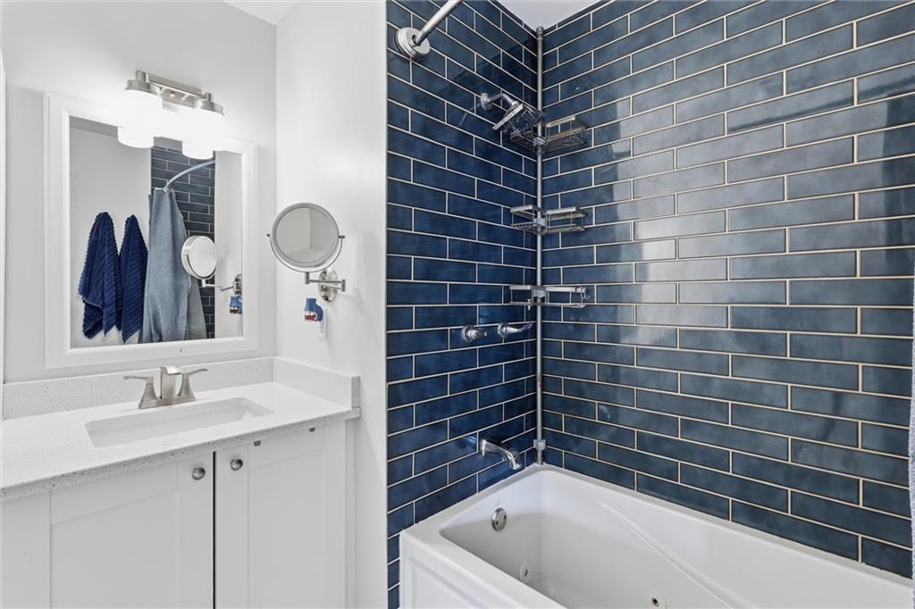 Bathroom with a white vanity beside a bathtub surrounded by dark blue subway tile.