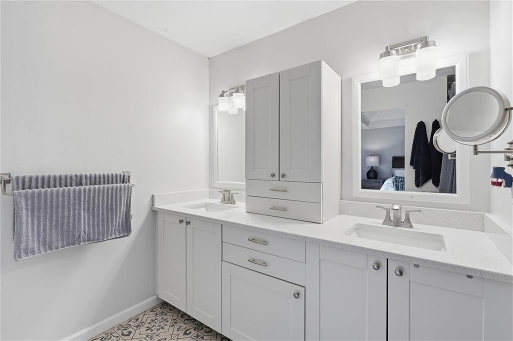 Bathroom with a white double-sink vanity, mirrored cabinets, and patterned tile floor.