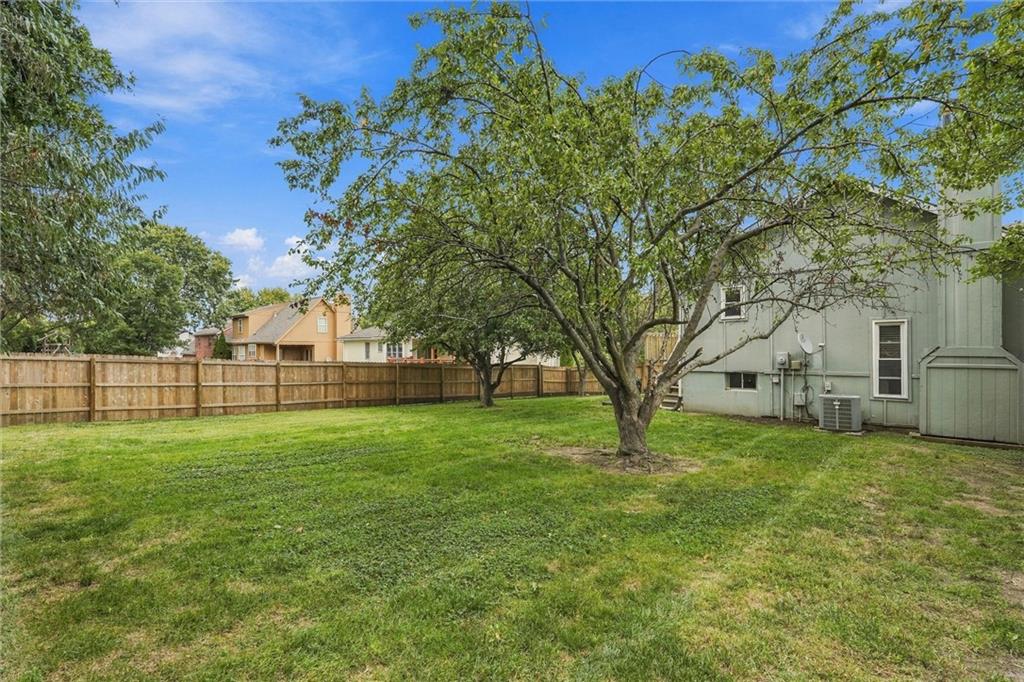 Fenced backyard with a broad lawn, mature trees, and a light-colored house.