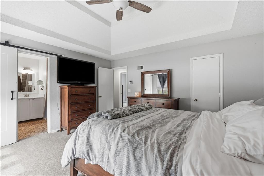 Bedroom with a large bed, tray ceiling, ceiling fan, and open doorway to the bathroom.